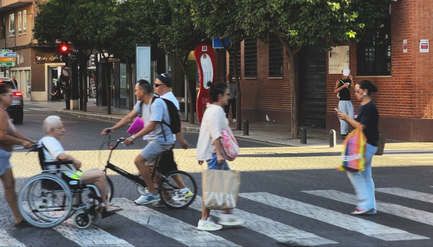 Vecinos cruzando un paso de peatones a pie, en bicicleta y en silla de ruedas